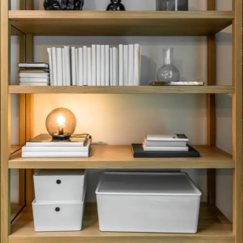 Modern book shelf featuring a minimalist wooden design with neatly arranged books, storage boxes, and decorative lighting